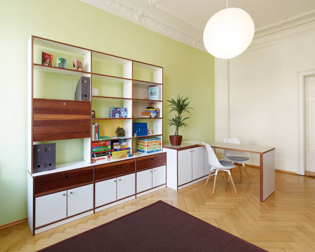 Regalsystem aus Holz mit verschiedenen Einrichtungsgegenständen, Massivholztisch mit zwei Stühlen und Kommode mit Zimmerpflanze