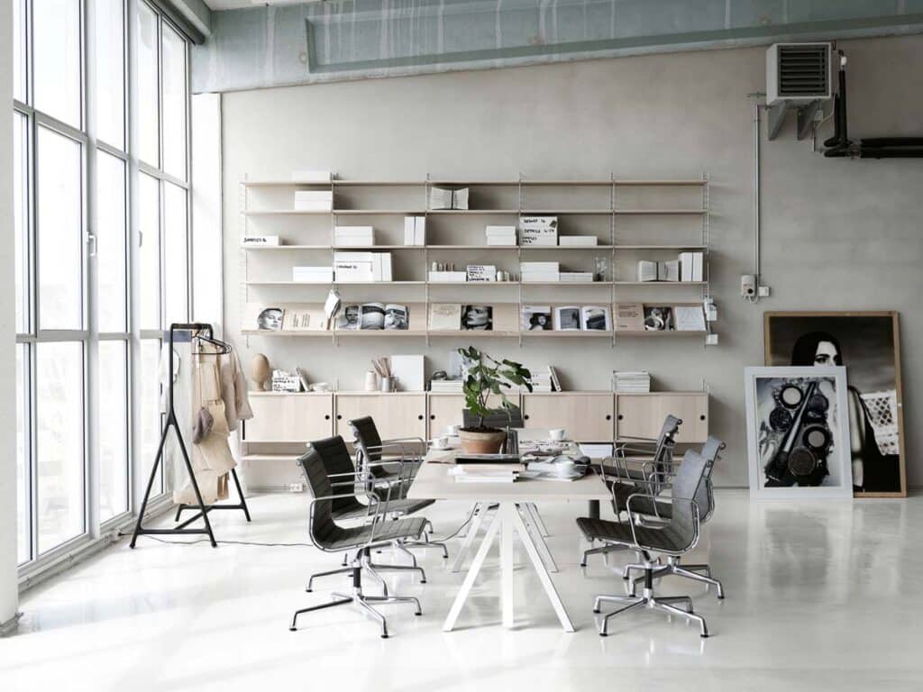 Eingerichtete Schrankwand aus Massivholz in einem studioähnlichen Bürogebäude mit großem Tisch und Bürostühlen sowie verschiedenen Bildern und einer großen Fensterfront